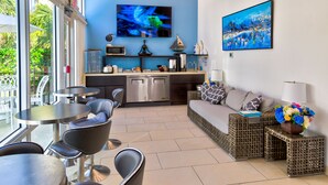 Une cuisine moderne équipée d’un téléviseur à écran plat, d’un coin repas avec chaises et tables, et d’un espace détente avec un canapé et des coussins.