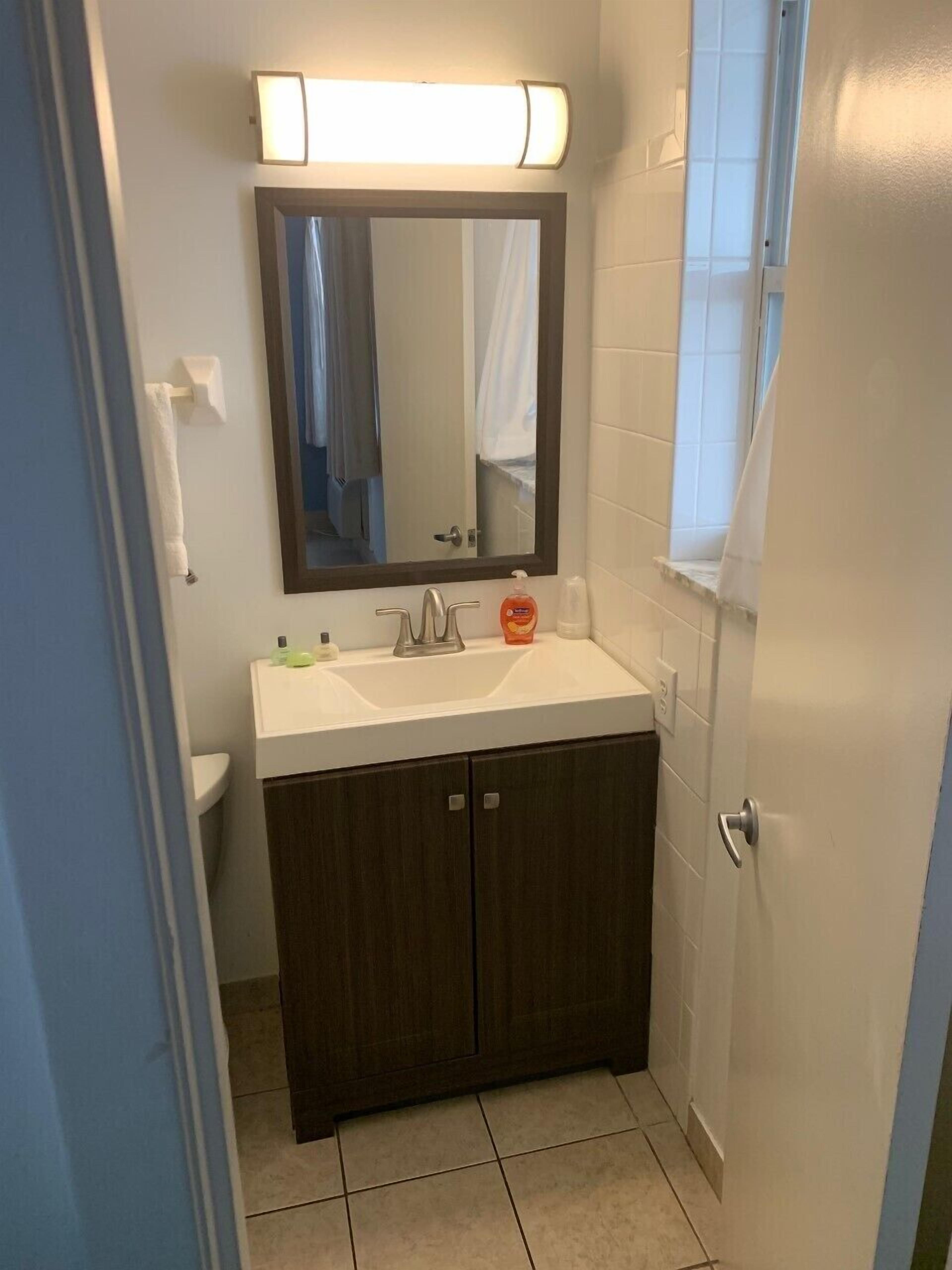 A bathroom with a white sink, dark wooden cabinets, a mirror with a light above it, and a white towel hanging on a rack.