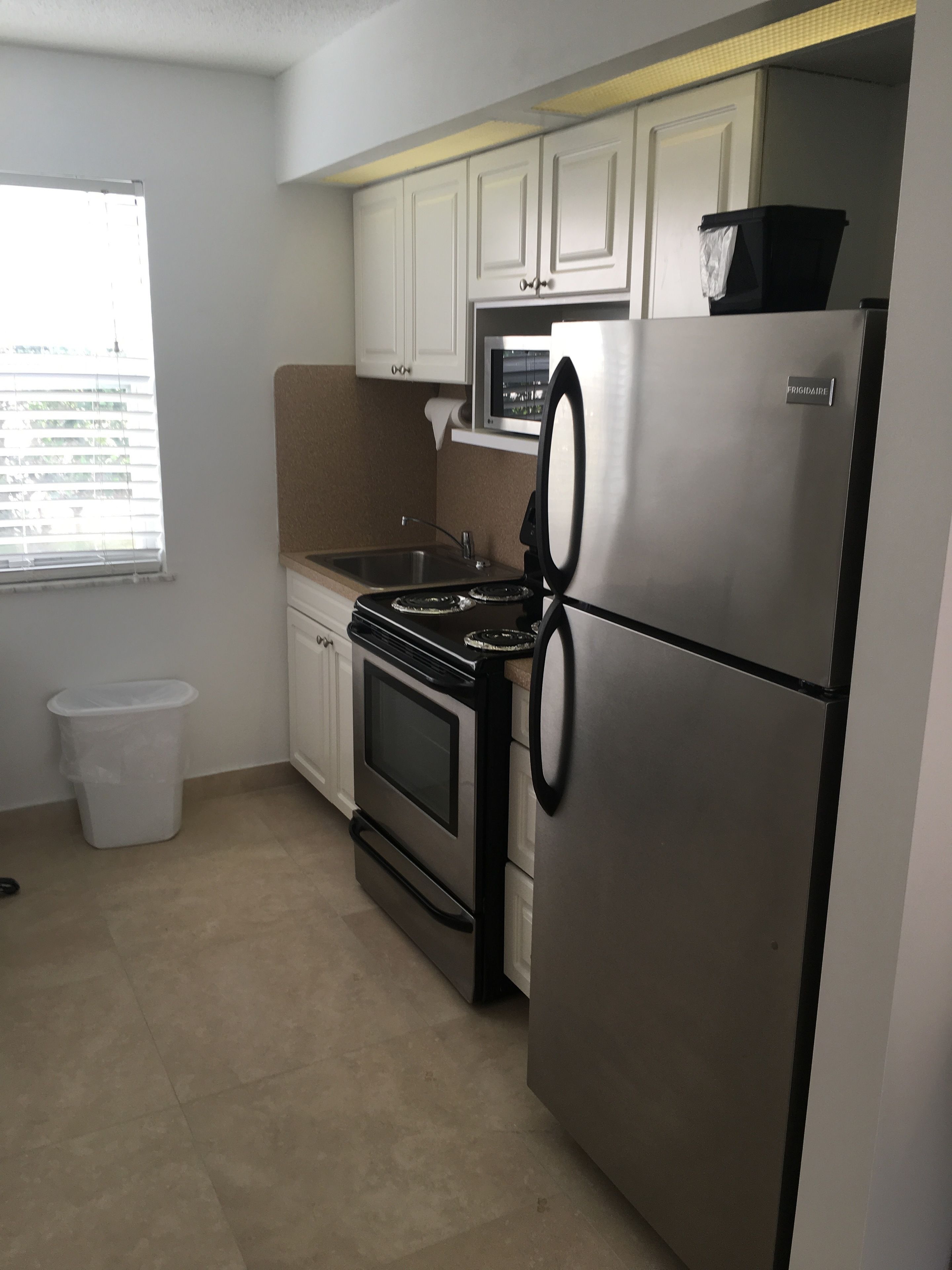 A compact kitchen with white cabinets, a stainless steel refrigerator, a microwave, and a stove.