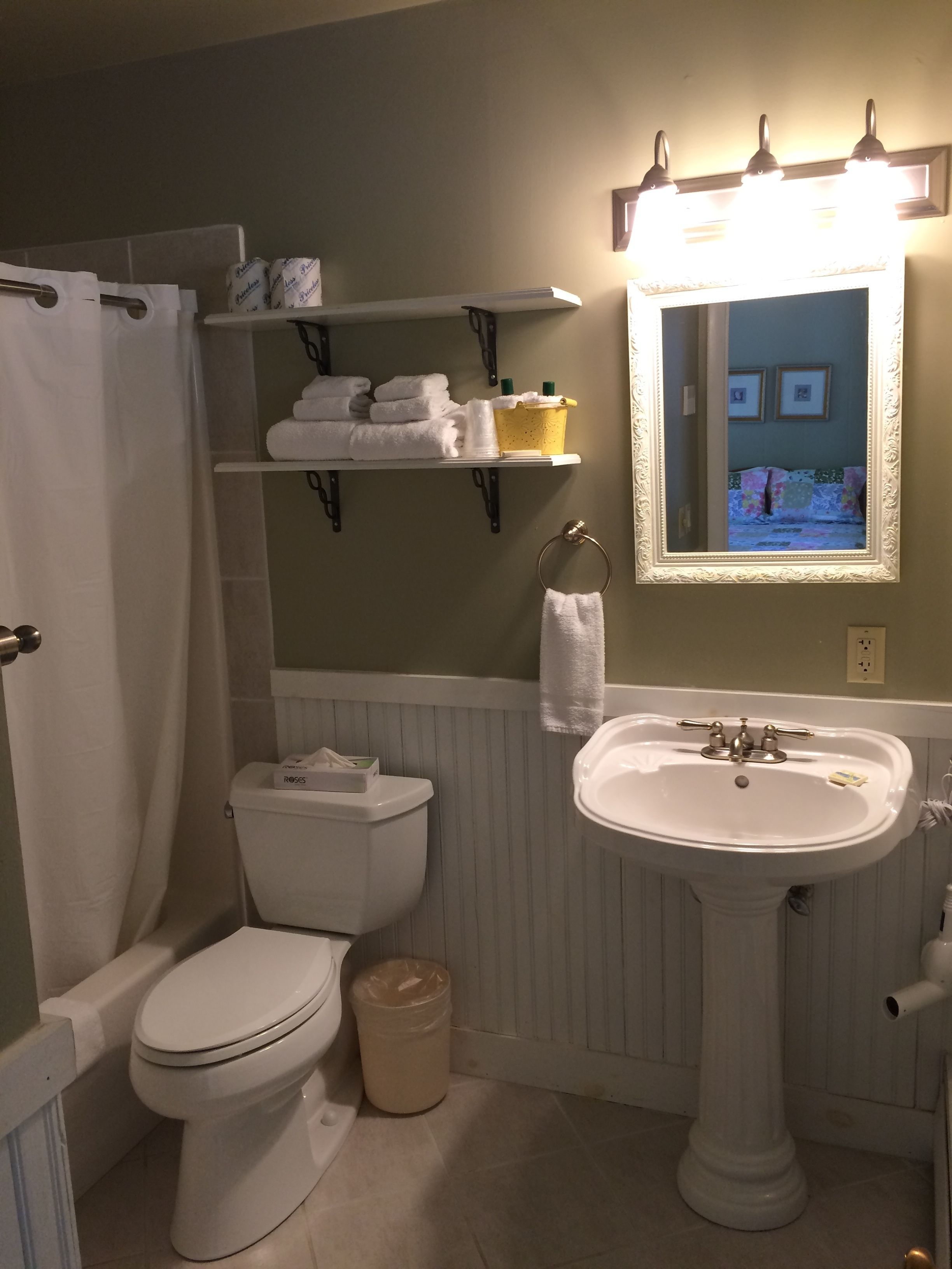A bathroom with a toilet, sink, and shower curtain. There are shelves above the toilet holding towels and toiletries.