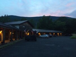 Un lodge rústico con zona de estacionamiento techada y montañas al fondo.