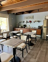 Un restaurante acogedor con mesas y sillas de madera, una zona de cocina y un letrero que dice 'GATHER' en la pared.