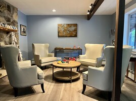 Una habitación con cuatro sillones de colores claros dispuestos alrededor de una mesa de centro de madera, una pared de piedra con un estante, y un mapa enmarcado en la pared.
