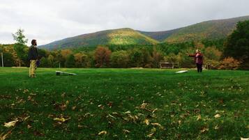 Um campo gramado com um banco e uma mesa, cercado por árvores e colinas.