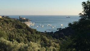Un paisaje costero con barcos, un barco y una estructura que parece un castillo sobre una colina.