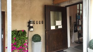Una puerta de madera con un panel de vidrio, un teléfono instalado en la pared y una maceta con flores rosadas.
