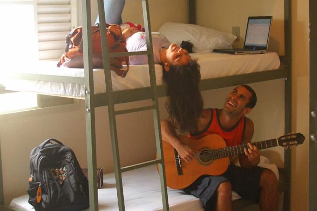 A bunk bed room with a laptop on the top bunk, a guitar on the bottom bunk, and a backpack on the floor.