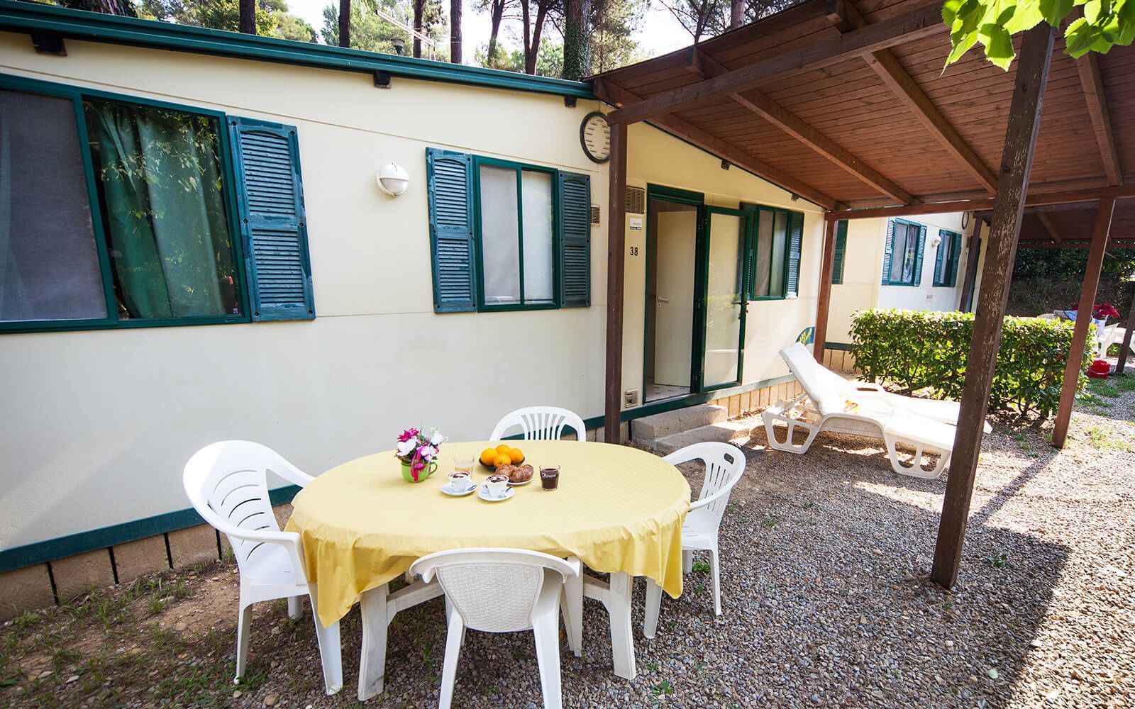 A covered outdoor dining area with a table set for two, surrounded by white chairs.