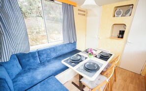A compact kitchenette with a blue sofa, a dining table set with plates and glasses, and a small refrigerator. - Toscana Holiday Village (Montopoli in Val d'Arno)