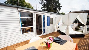 Casa móvil con un patio amueblado que incluye una mesa para dos, asientos exteriores y una zona cubierta con cortinas.