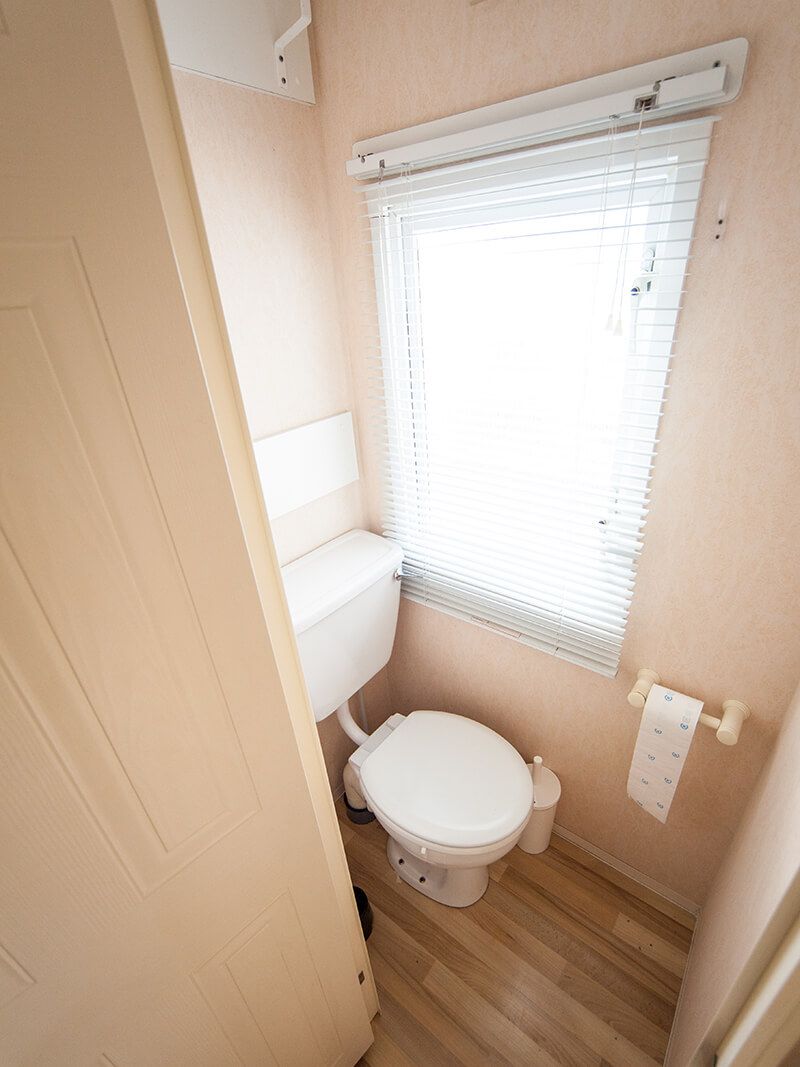 A compact bathroom with a toilet, a window with blinds, and a towel rack.