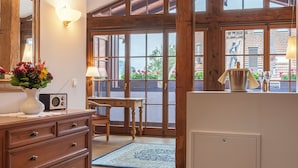 Een kamer met houten balken, een groot raam, een dressoir, een radio en een tafel met een lamp.