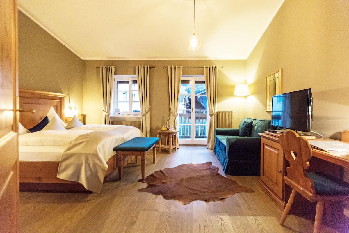 A hotel room with a bed, a desk, a television, a chair, a sofa, and a view of the outdoors through the windows.