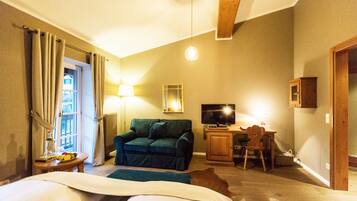 A hotel room with a bed, a green sofa, a television, a desk, and a chair.