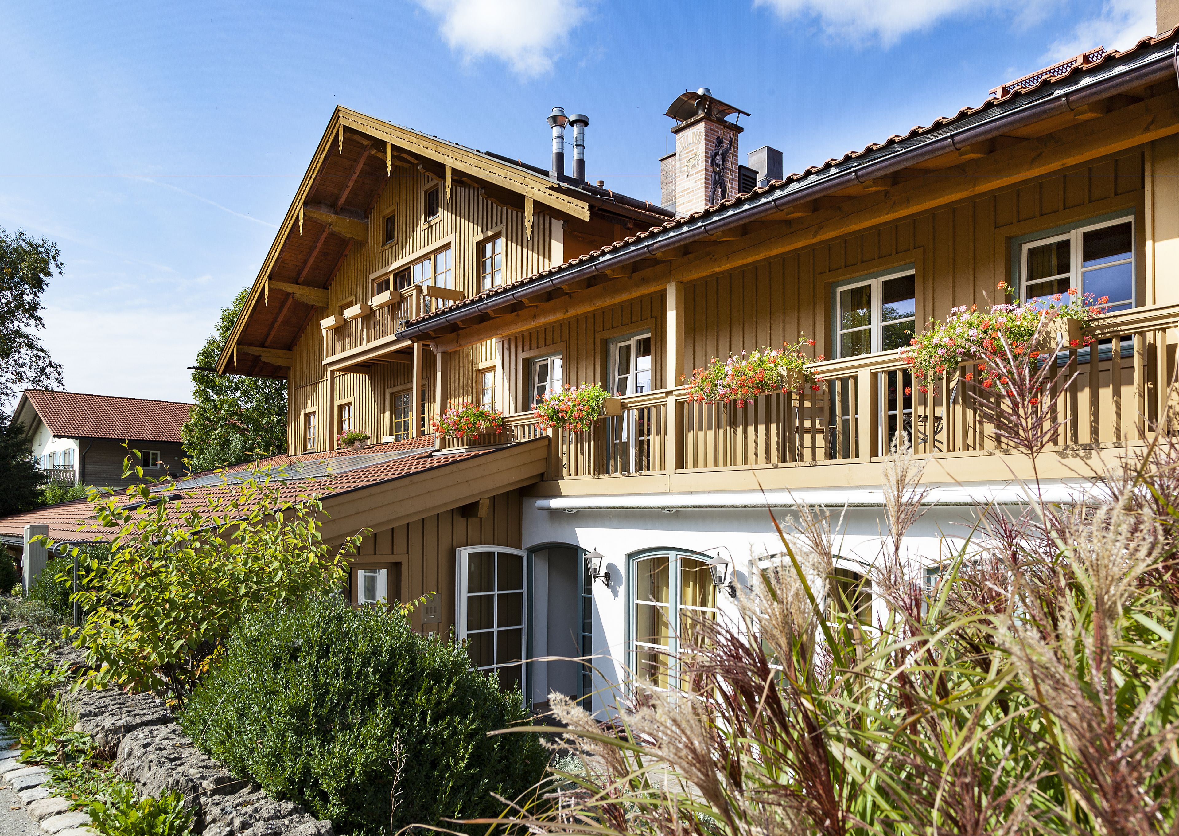 A two-story wooden house with a balcony, large windows, and a chimney.