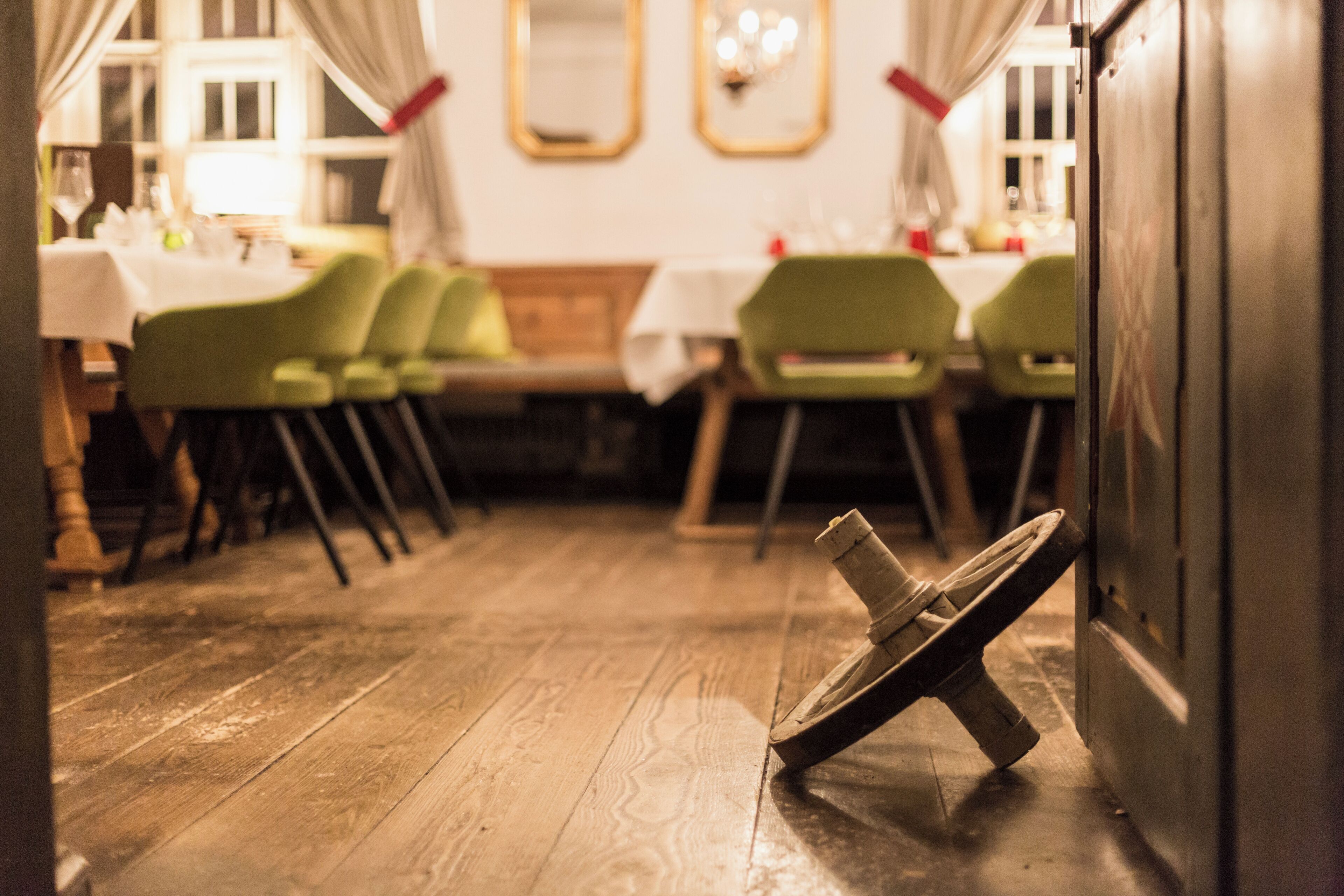 Een eetgedeelte met houten vloer, groene stoelen en gedekte tafels.