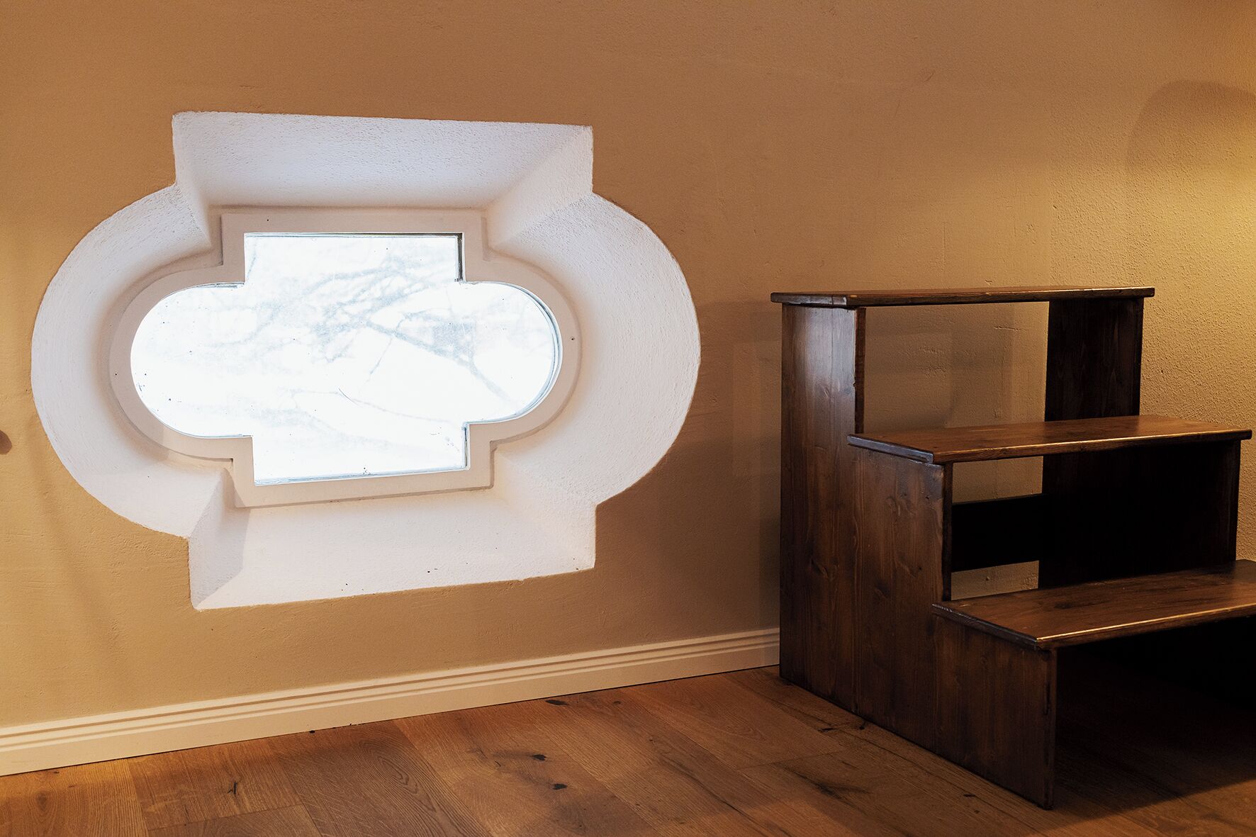 A room with a unique wall design featuring a circular window and a wooden shelving unit.