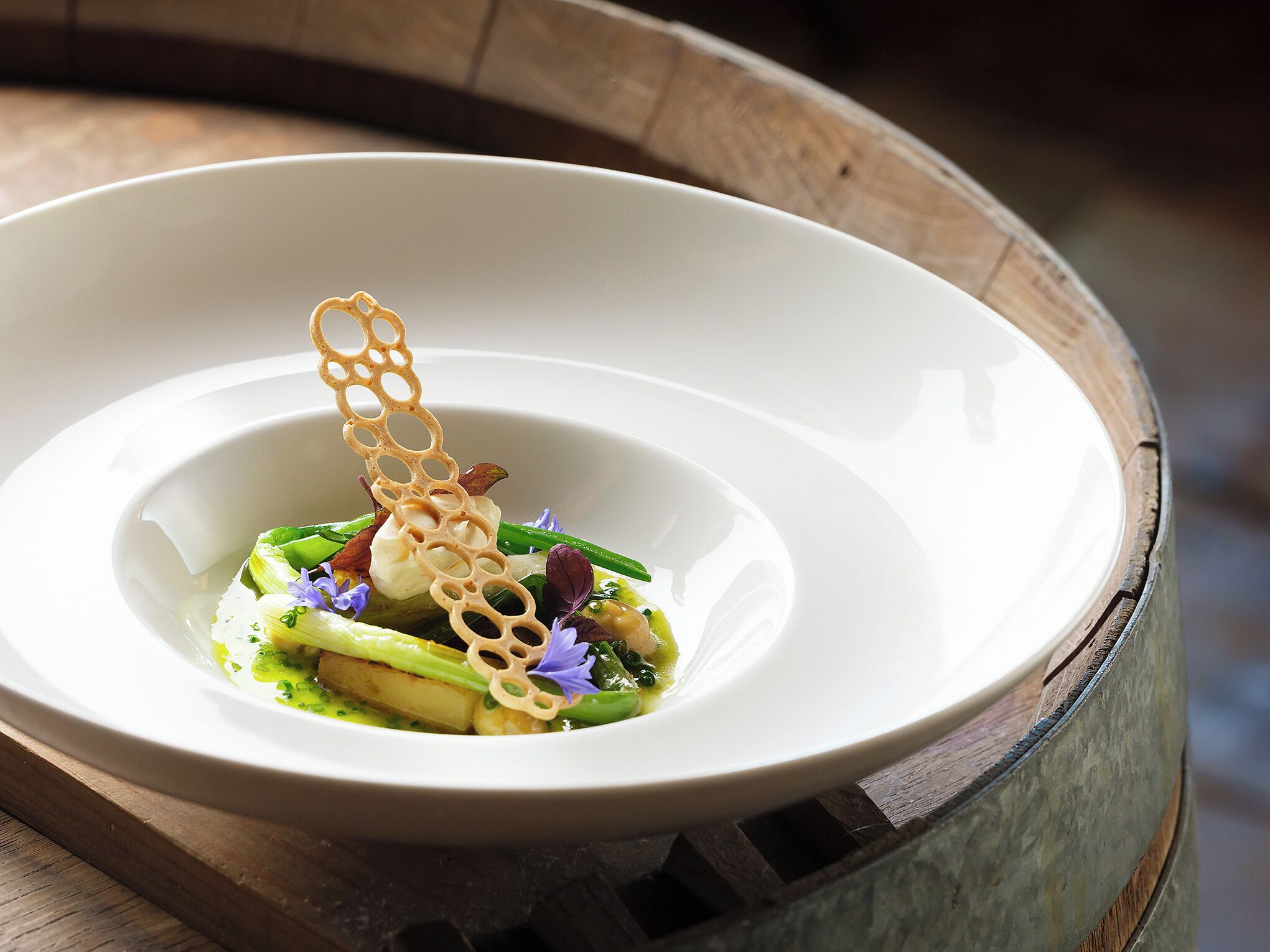A white bowl with a wooden base, containing a dish with green vegetables and a decorative element.