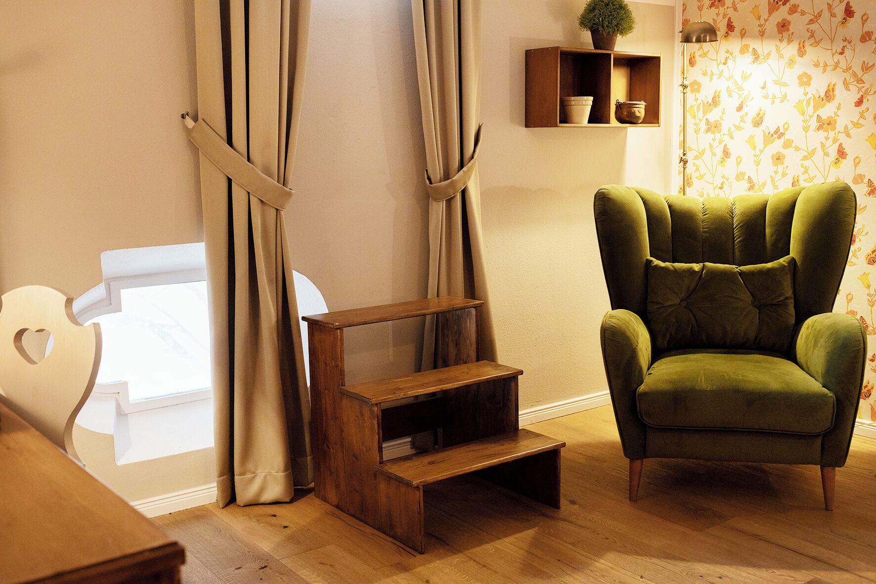 A room with a green armchair, wooden steps, and a shelf with decorative items.
