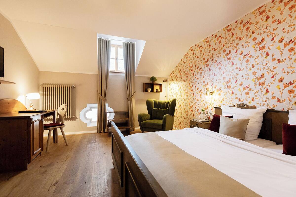 A bedroom with a large bed, a desk with a chair, a green armchair, and a radiator.