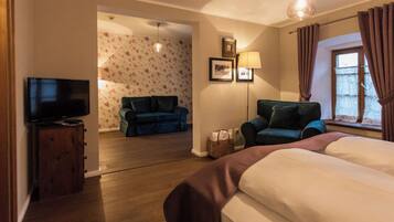 A hotel room with a bed, a television, a sofa, a chair, a lamp, and a window with curtains.