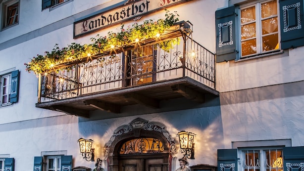 Een gebouw met een bord waarop 'Landgasthof Harner' staat, een balkon met lichtslingers en een standbeeld op de begane grond.