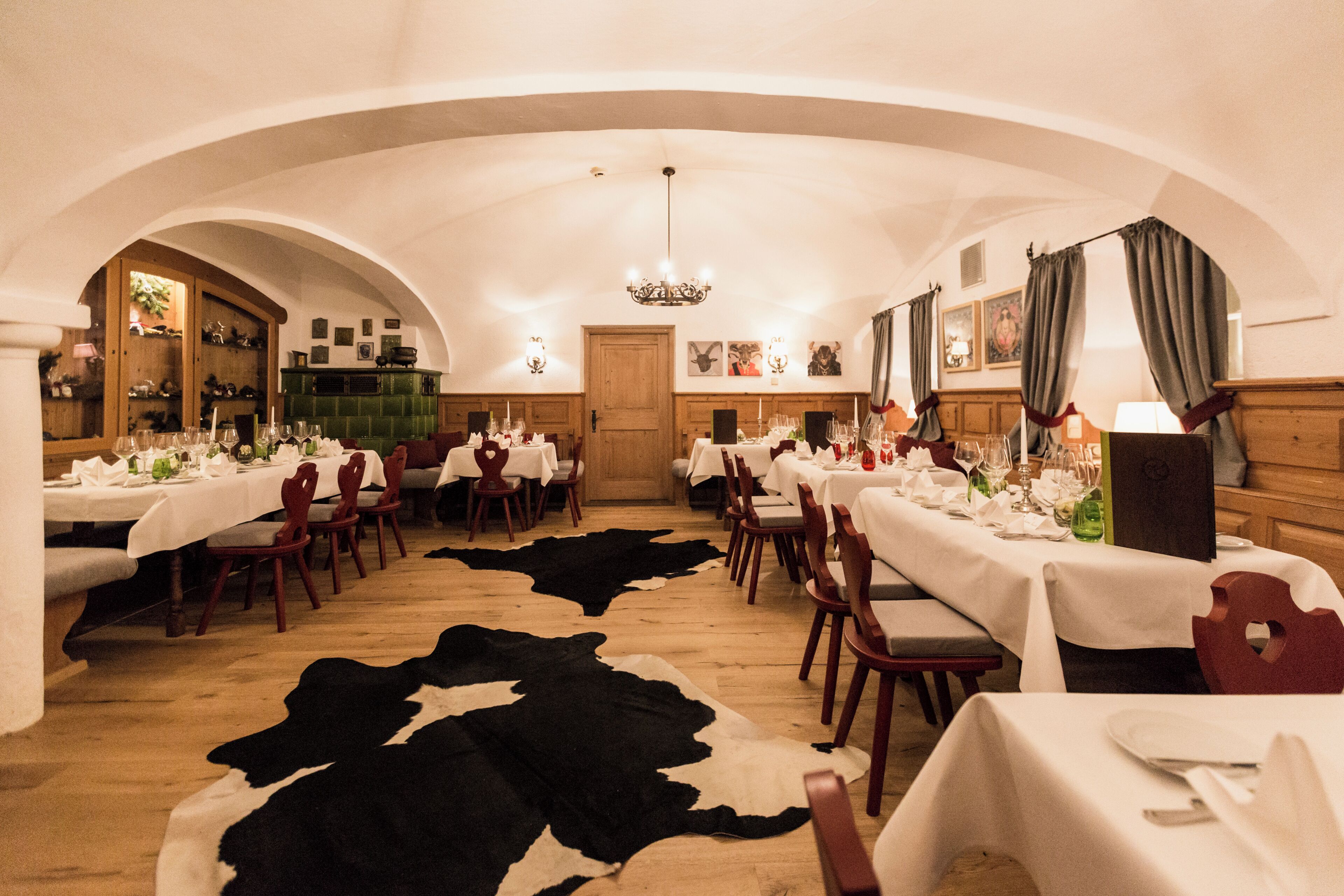 Un comedor con mesas dispuestas para una comida, sillas de madera, una araña y un tapiz de cuero de vaca en el suelo.