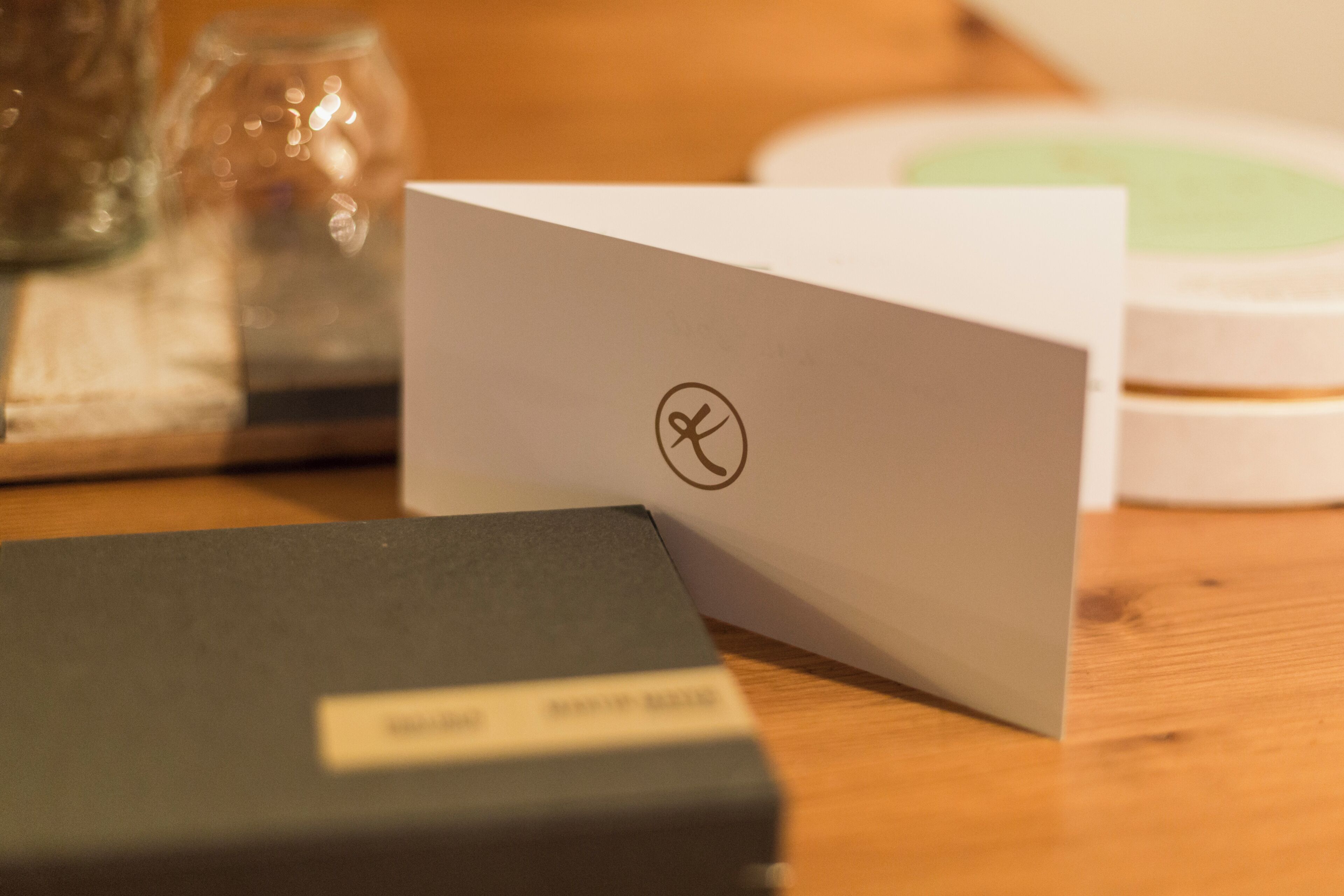 Una mesa de madera con una tarjeta blanca, una caja negra y un tarro de vidrio.