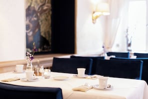 Une table à manger dressée avec de la vaisselle blanche, un vase rempli de fleurs et un tableau accroché au mur.