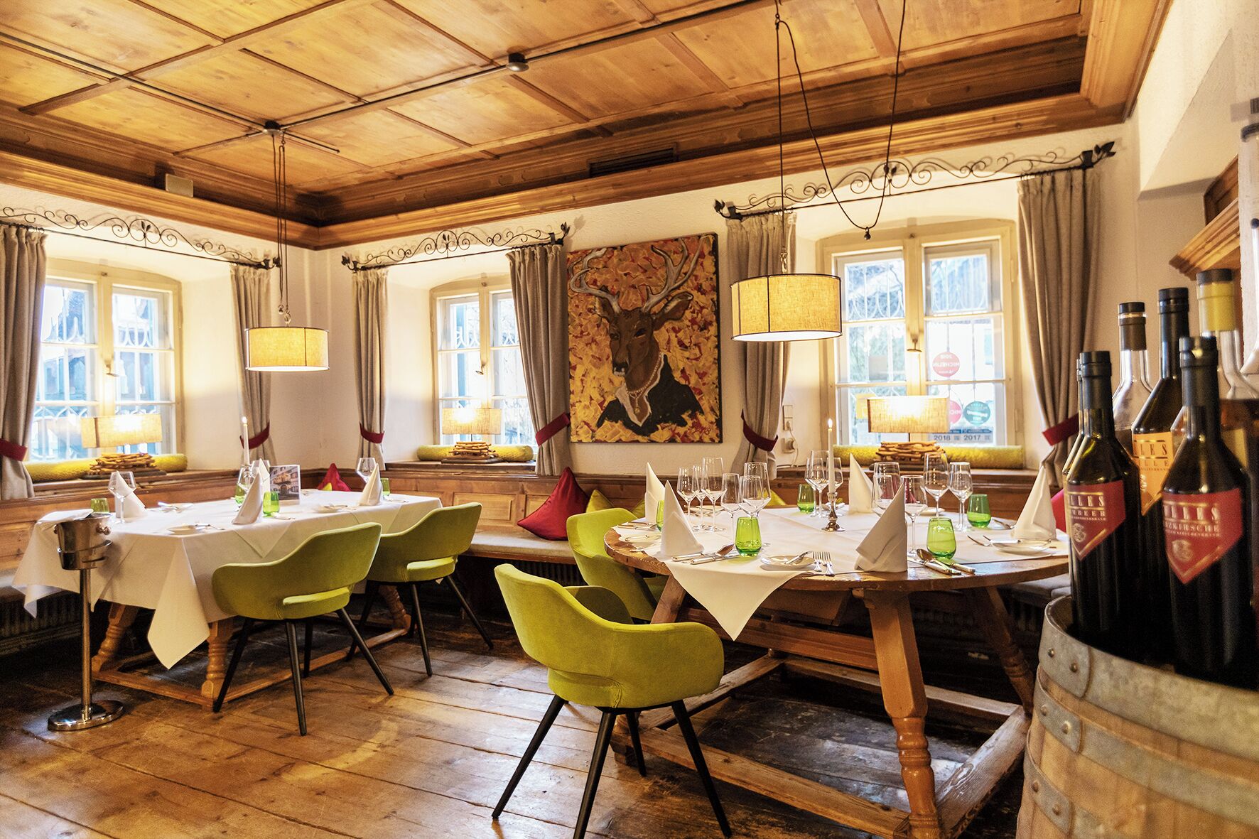 Un restaurante con suelos de madera, sillas verdes, manteles blancos y botellas de vino.