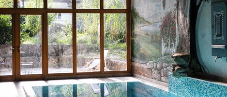 Una piscina con agua cristalina, ventanas amplias y un mural de un paisaje.
