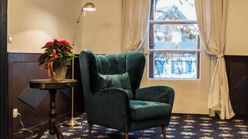 A room with a green armchair, a small table with a potted plant, a floor lamp, and a window with curtains.