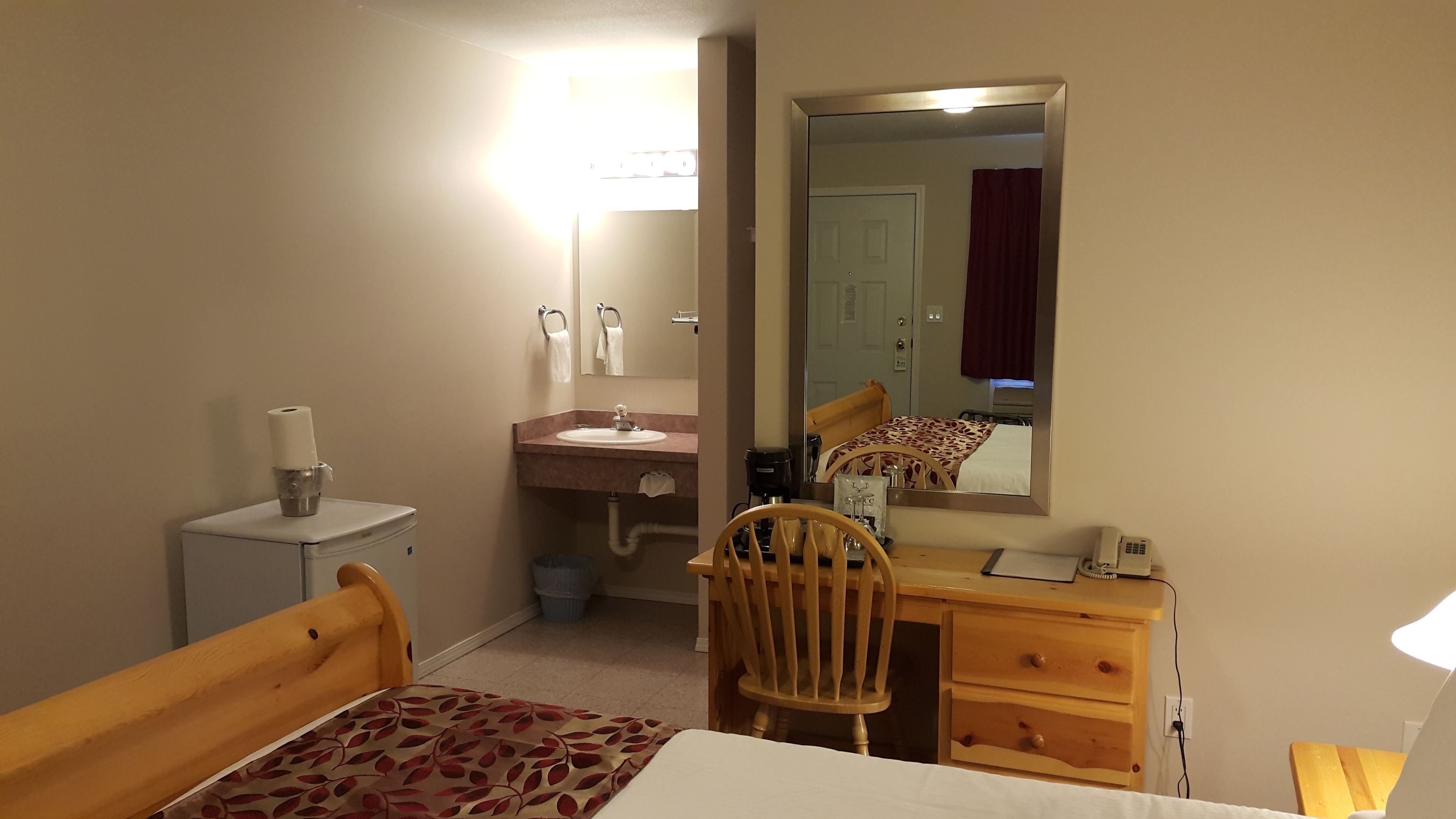 Habitación de hotel con una cama, un escritorio con silla, tocador con espejo, lavamanos y un inodoro.