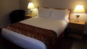 A neatly made bed with a patterned throw, two bedside lamps, a wooden nightstand, and a chair.