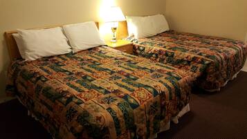 Una habitación de hotel con dos camas, cada una con una colcha estampada y almohadas blancas. Entre las camas hay una mesita de noche con una lámpara.