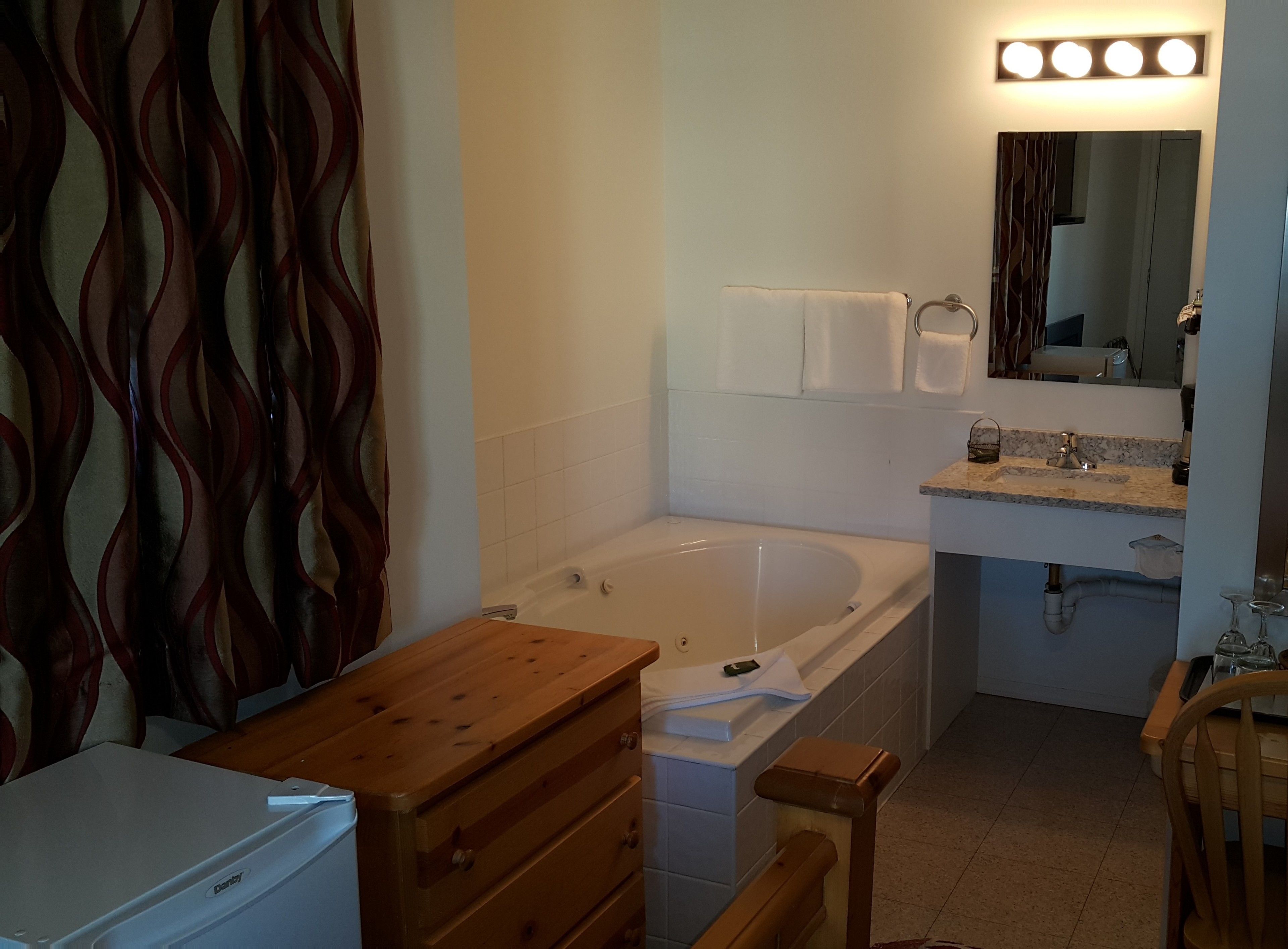A bathroom with a bathtub, a vanity with a mirror, and a wooden bench.