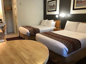 A hotel room with two beds, a round wooden table, a nightstand, and a framed picture on the wall.