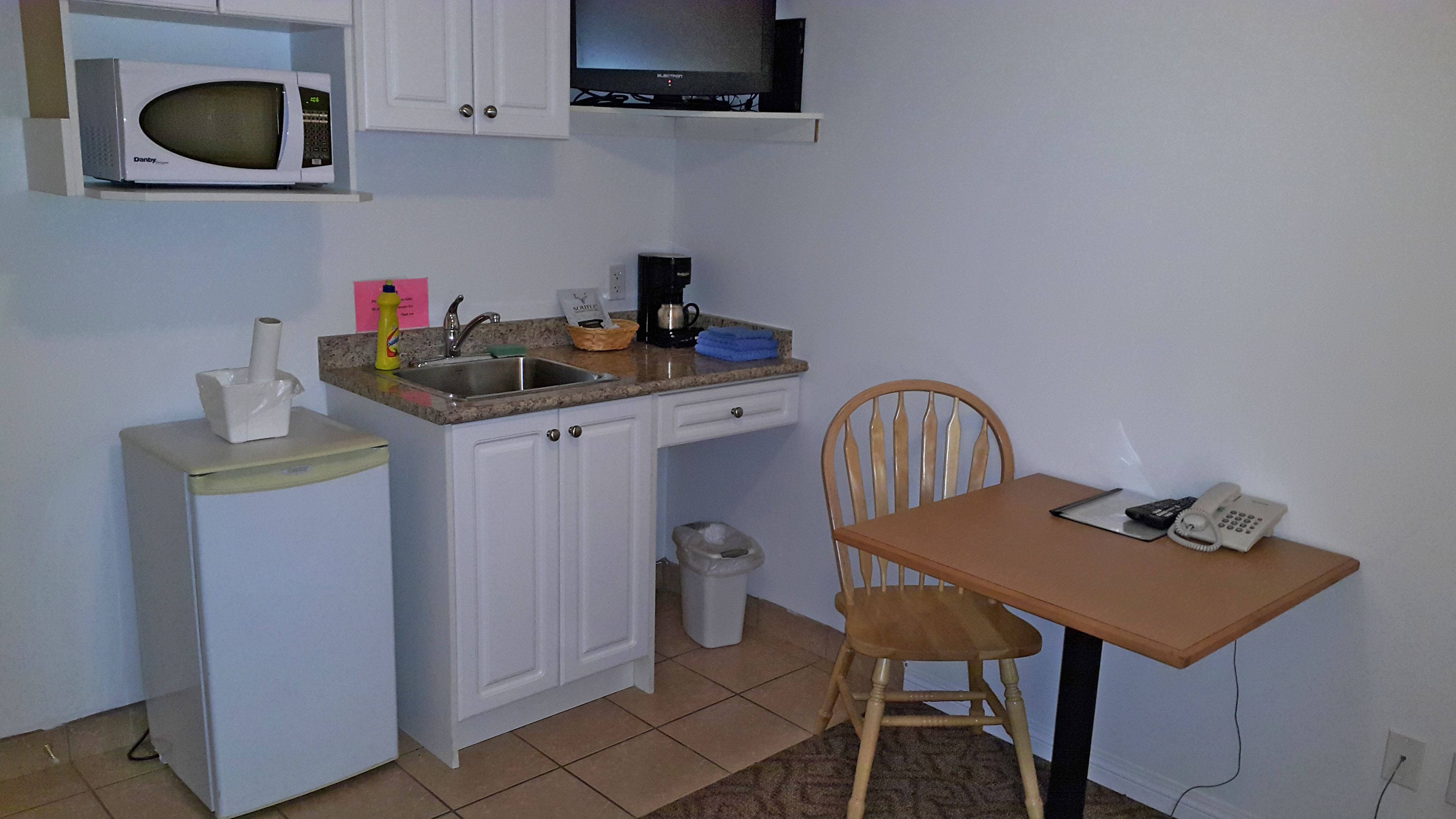 A compact kitchen with a microwave, sink, and a small table with a chair.