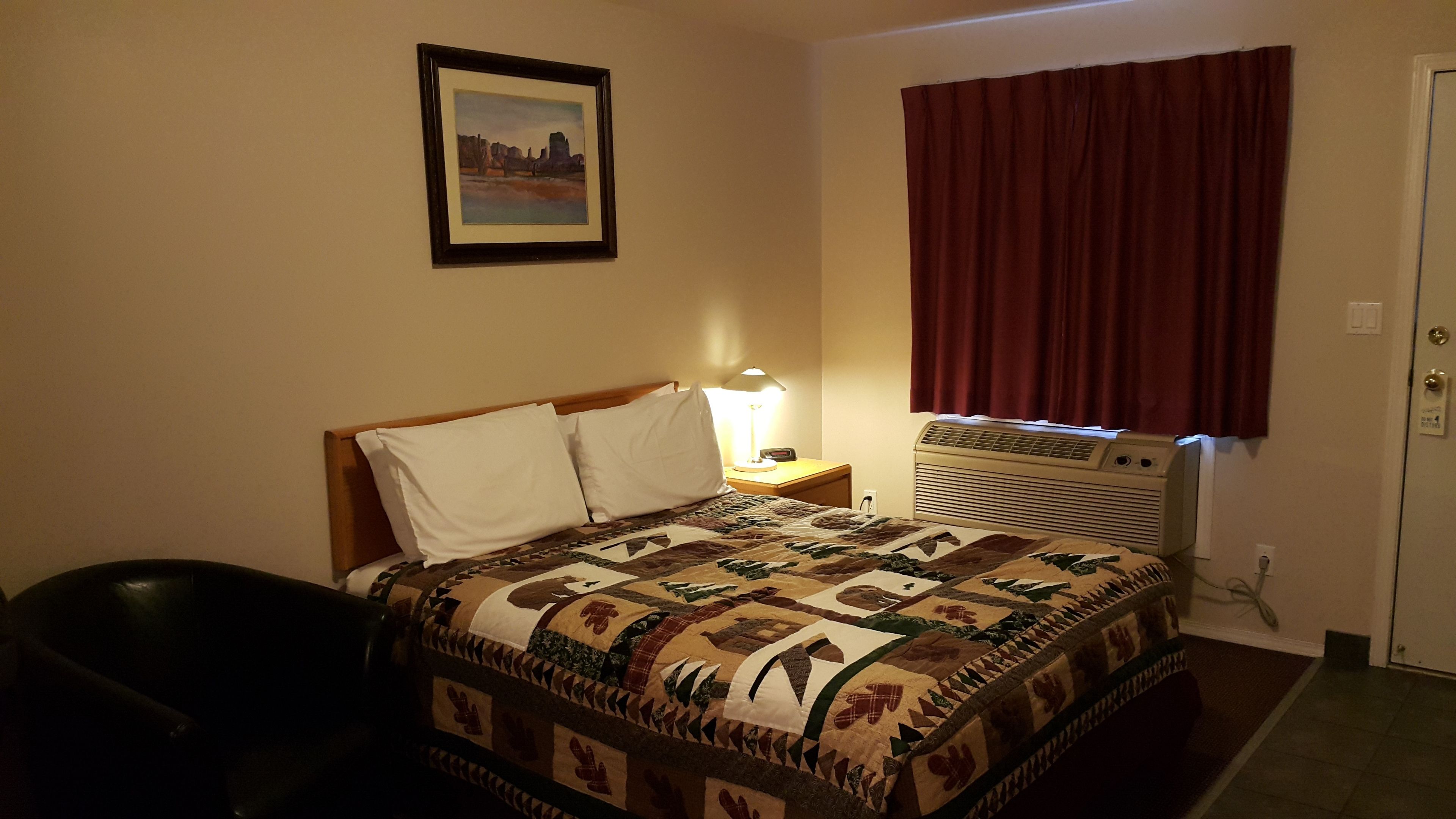 A hotel room with a bed, a nightstand, a lamp, a heater, and a window with curtains.