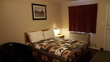 A hotel room with a bed, a nightstand, a lamp, a heater, and a window with curtains.