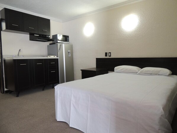 A hotel room with a bed, a kitchenette, and a nightstand.