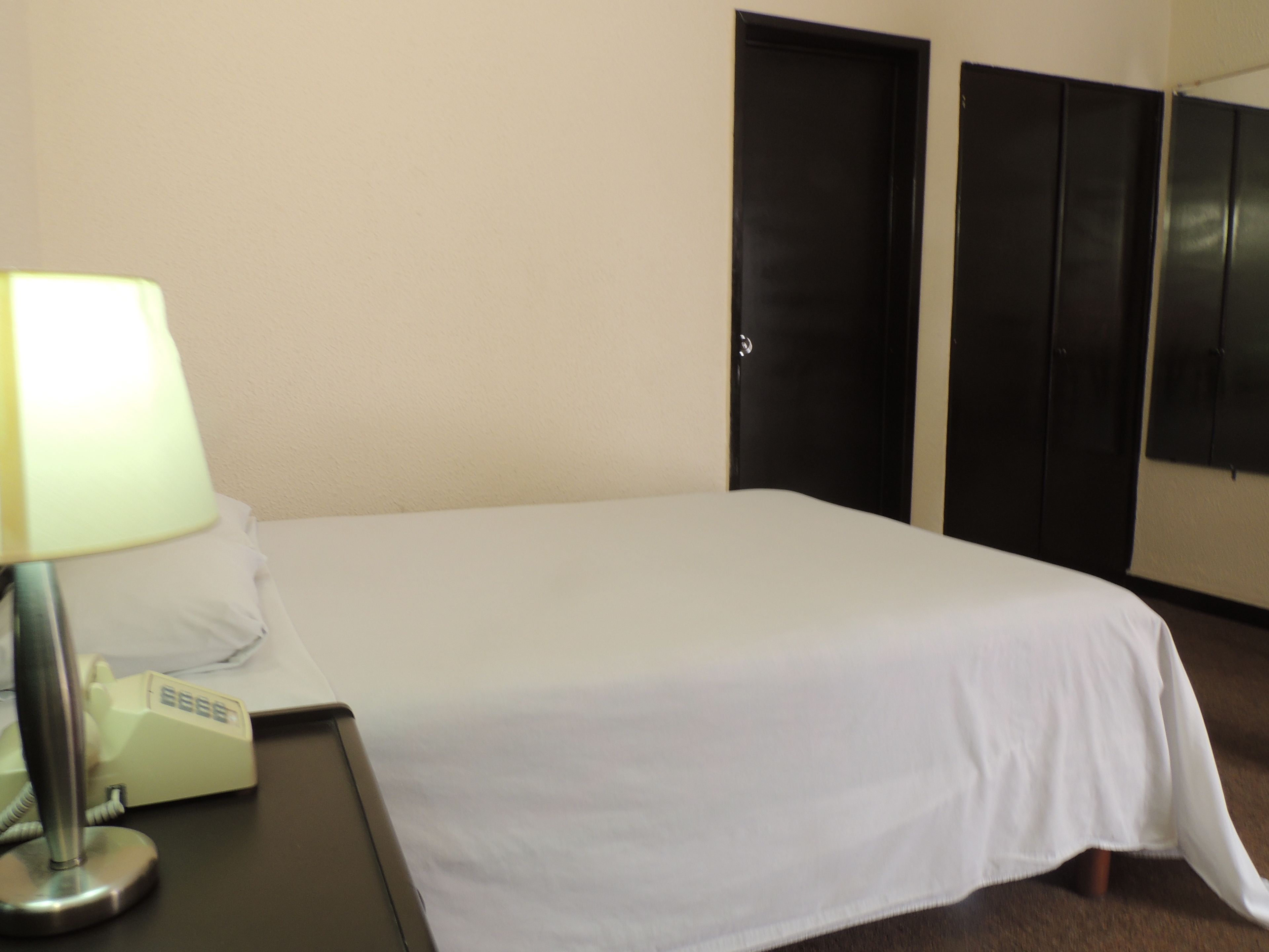 A hotel room with a bed, a lamp, a telephone, and two doors.
