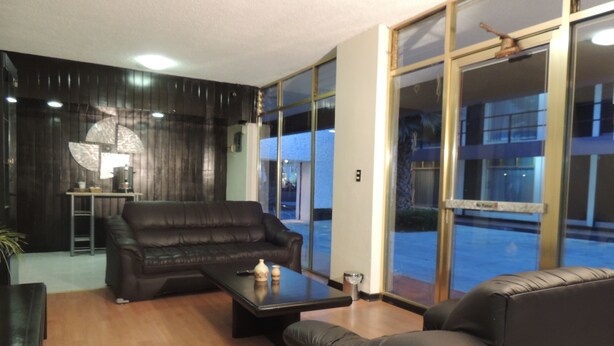 Un moderno salón con un sofá de cuero negro, una mesa de centro y una lámpara. Hay un ventanal con vistas al exterior.