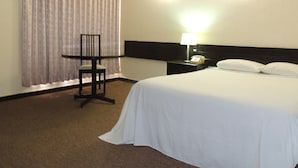 Habitación de hotel con cama, escritorio, silla, mesita de noche con lámpara y teléfono.
