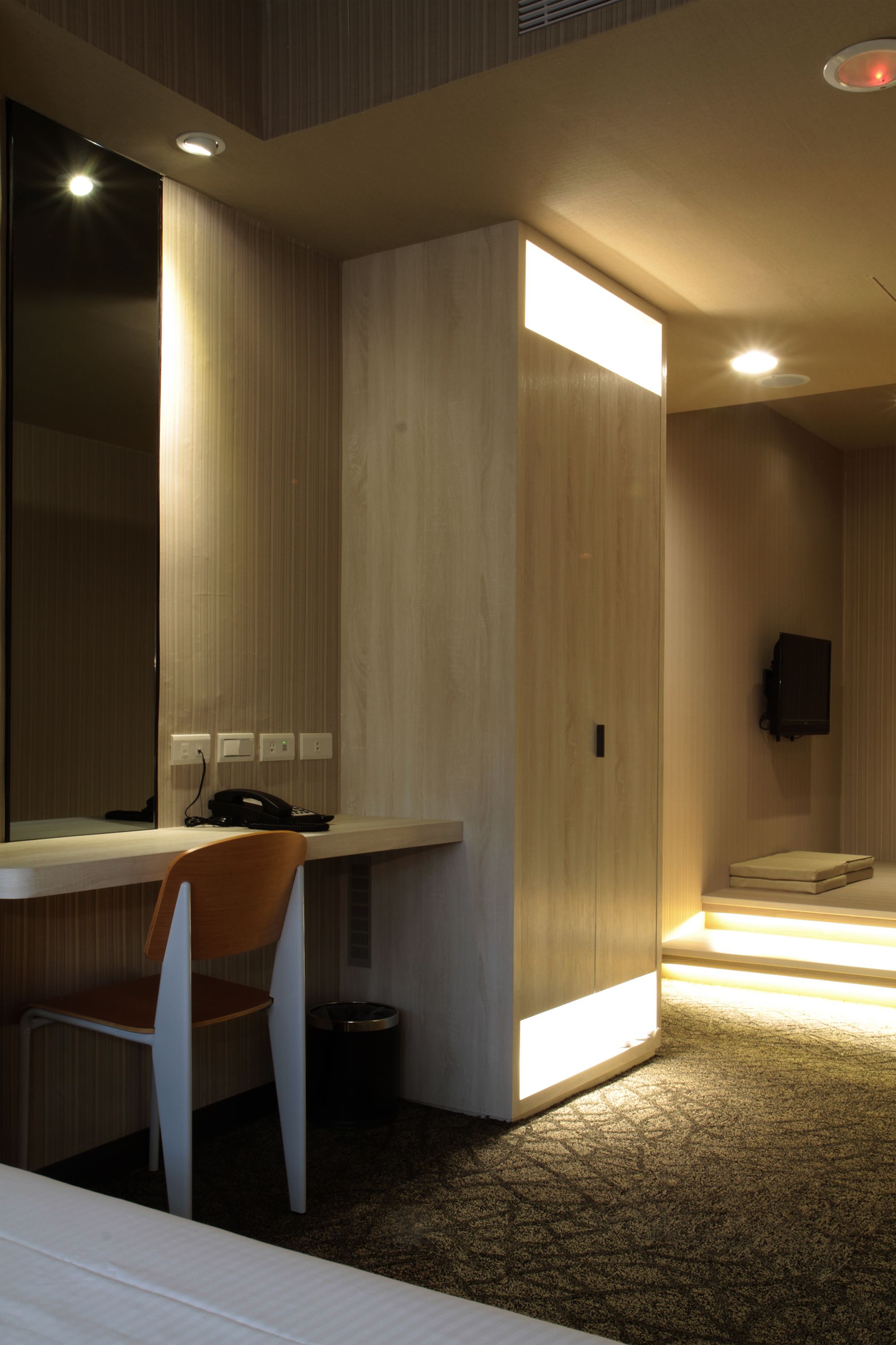 Een moderne hotelkamer met een houten bureau, een stoel, een bed, een televisie en een kleine prullenbak.