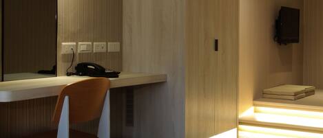 Een moderne hotelkamer met een houten bureau, een stoel, een bed, een televisie en een kleine prullenbak.