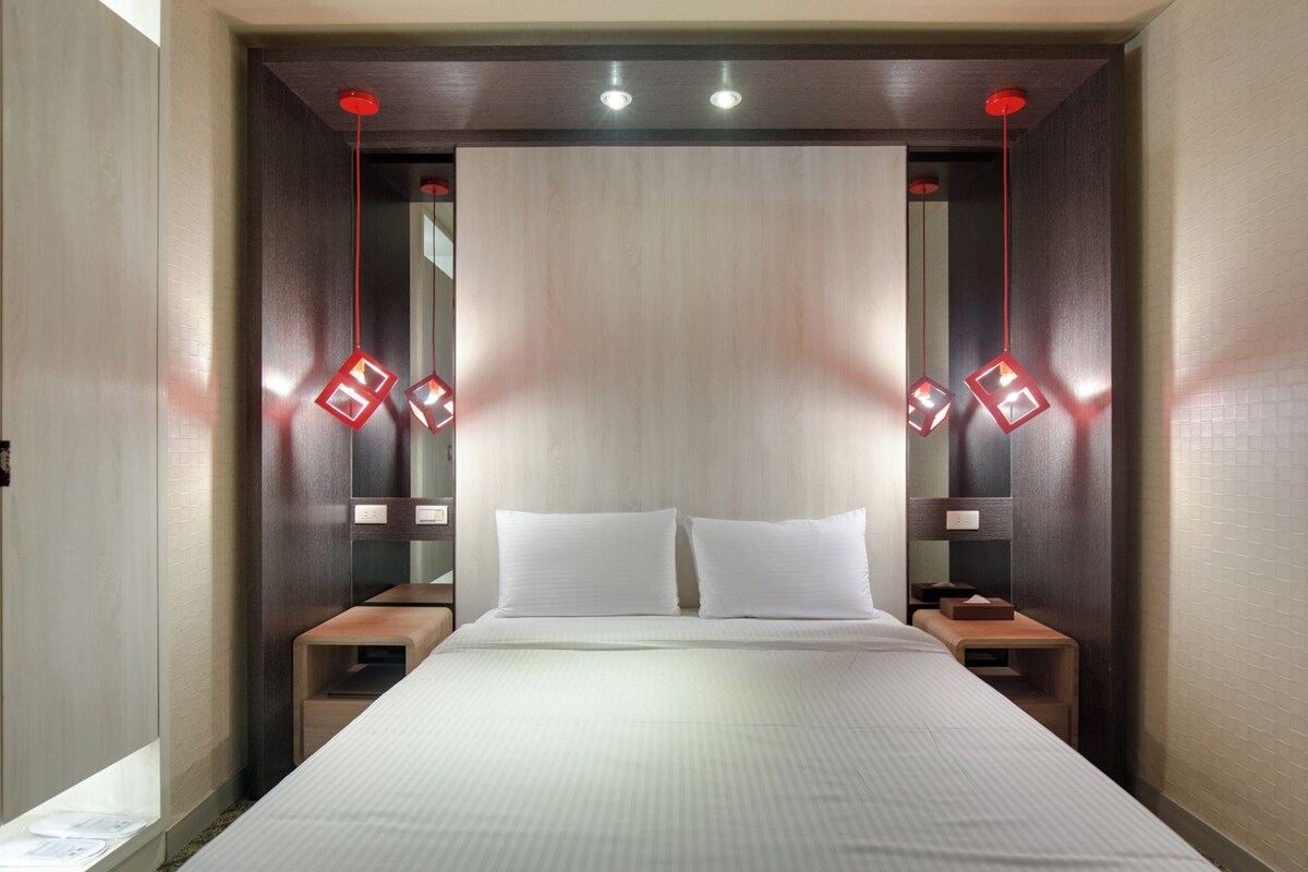 A hotel room with a large bed, two bedside tables, and a headboard with integrated lighting.