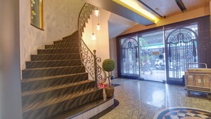 A staircase with a decorative railing, a small potted plant, and a luggage cart near a glass door leading outside. - East Dragon Hotel (Taipei)