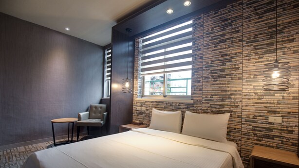 A modern hotel room with a large bed, a small desk, a chair, and a window with blinds. - East Dragon Hotel (Taipei)