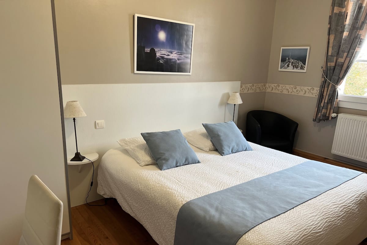 Un dormitorio ordenado con una cama grande, dos lámparas de noche, una silla y un radiador.